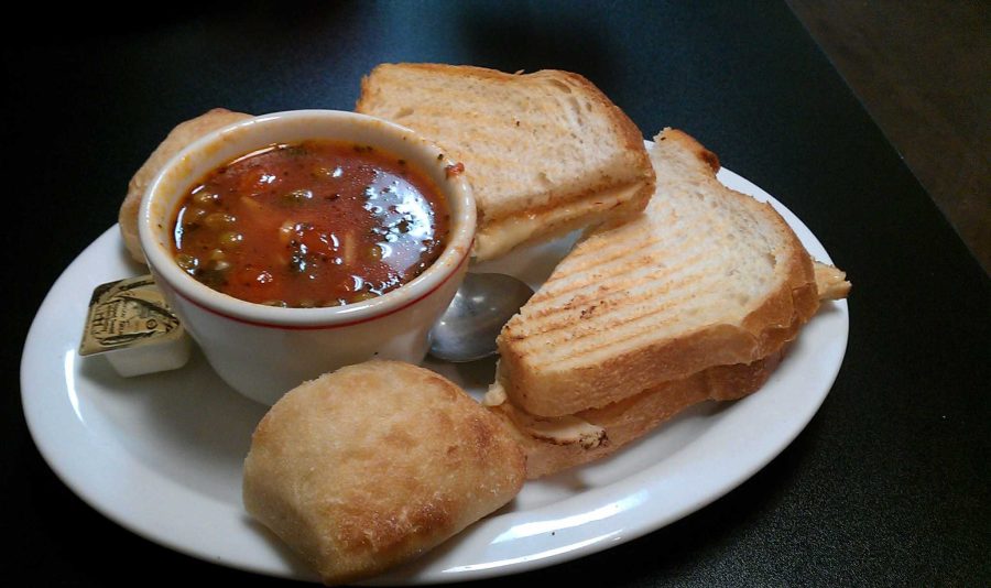 A grilled turkey panini accompanied by a bowl of vegetable minestrone soup from Bravos Soup and Sandwich Shoppe.