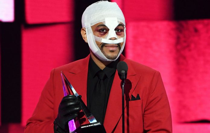The Weeknd accepting an award at the American Music Awards. His face is bandaged and beaten as he's still playing the character from his "After Hours" persona.