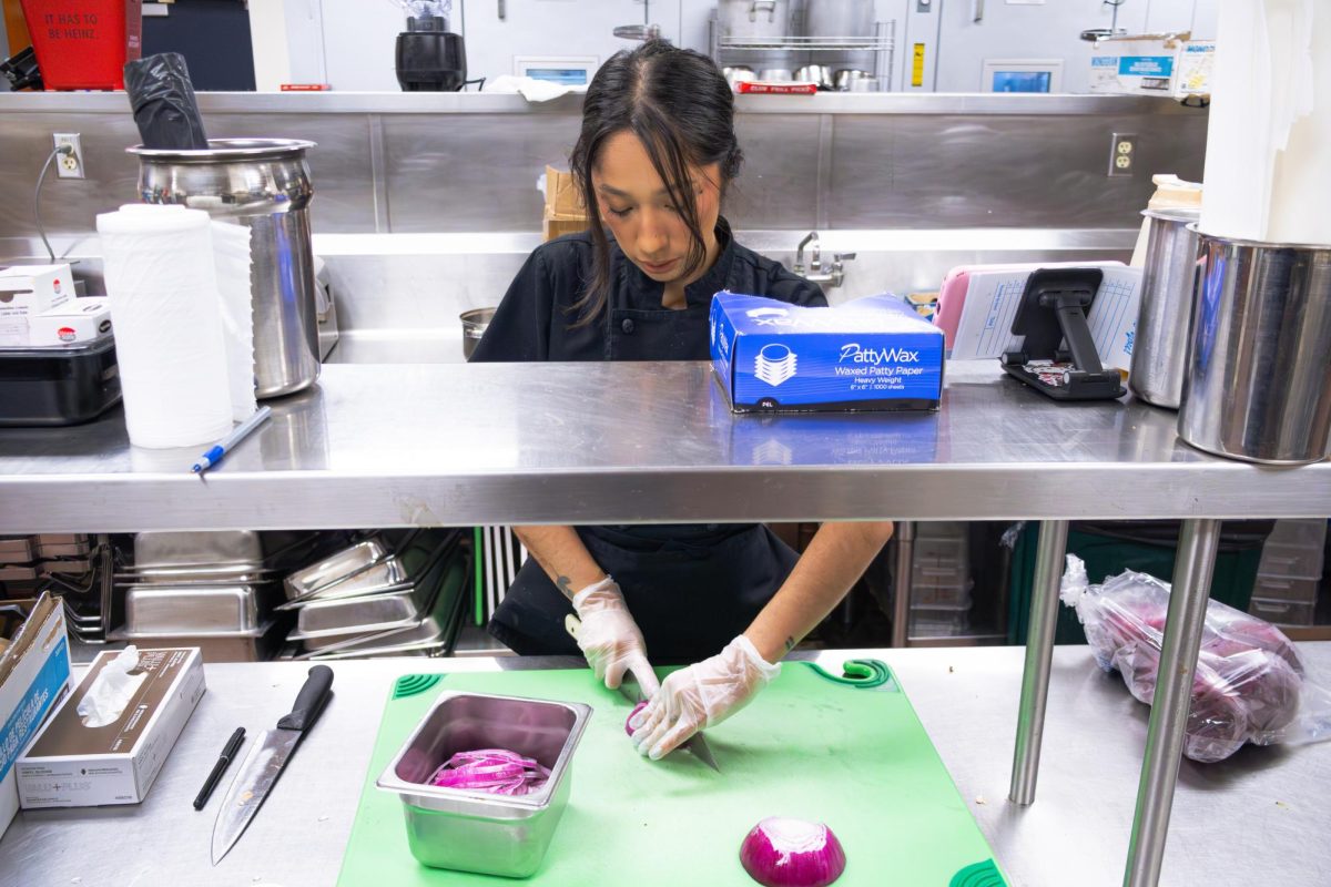 Victoria Estrada, a 26-year-old general manager of food services, cutting onions to prepare for the sandwich station before the cafeteria opens for the day on April 10. Estrada said she comes in between one to three hours before the cafeteria opens to prep for the day depending on if she has catering orders to fulfill. She joined the team in February as a transfer from Sacramento City College, where she was also the general manager. Estrada oversees all services, including the Hawkeye Grill and the Oasis Cafe and handles all the catering requests.